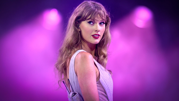 Taylor Swift appears onstage surrounded by purple. She wears a purple bodysuit.